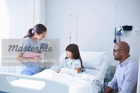 Female nurse explaining to girl patient with arm plaster cast in hospital children's ward with father Female nurse explaining to girl patient with arm plaster cast in hospital children's ward with father