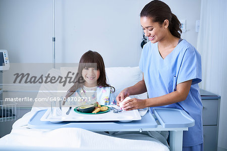 Female nurse serving lunch to girl patient with arm plaster cast in hospital children's ward Female nurse serving lunch to girl patient with arm plaster cast in hospital children's ward