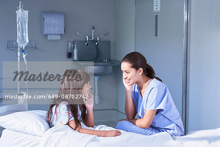 Nurse talking with girl patient sitting up in bed on hospital children's ward