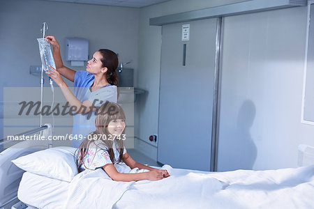 Nurse adjusting intravenous drip for girl patient in bed on hospital children's ward Nurse adjusting intravenous drip for girl patient in bed on hospital children's ward