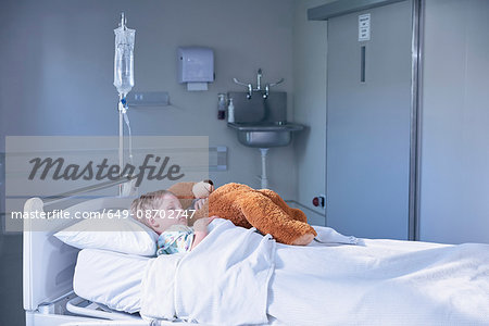 Boy patient in bed hugging teddy bear on hospital children's ward