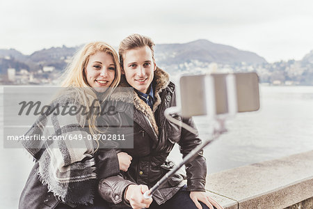 Young couple taking smartphone selfie on harbour wall, Lake Como, Italy