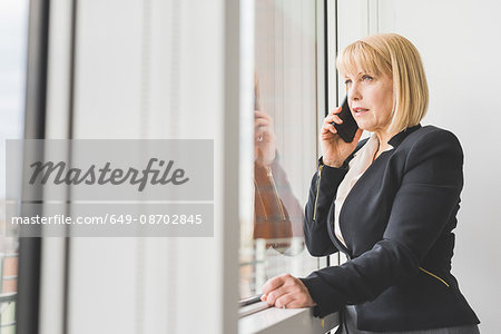 Mature businesswoman talking on smartphone at office window