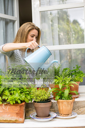 Woman watering herb plants on windowsill