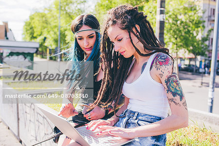 Two young women typing on laptop in urban park