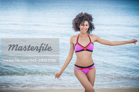 Beautiful young woman wearing pink bikini dancing on beach, Costa Rei, Sardinia, Italy