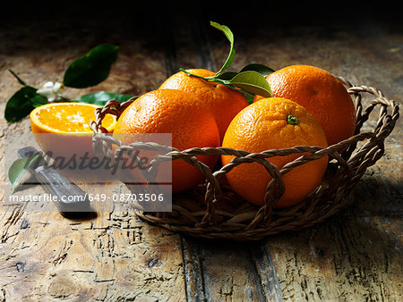 Oranges in basket with one halved in background, rustic wooden table