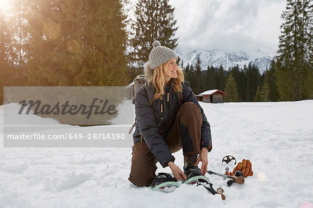 Mature woman putting on snow shoes in snowy landscape, Elmau, Bavaria, Germany