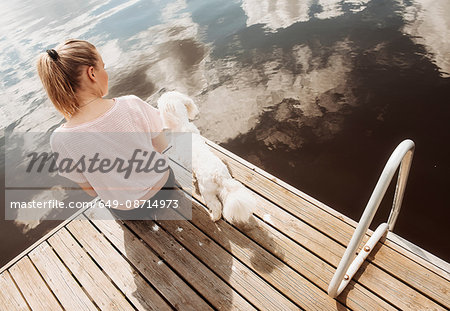 Woman sitting with Coton de tulear dog on lake pier, Orivesi, Finland