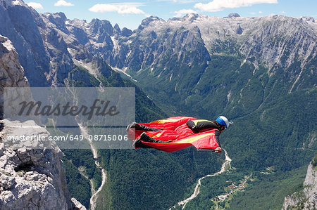 Wingsuit BASE jumper flying along cliff side and down the valley, Italian Alps, Alleghe, Belluno, Italy