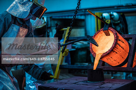 Male foundry workers pouring bronze melting pot in bronze foundry