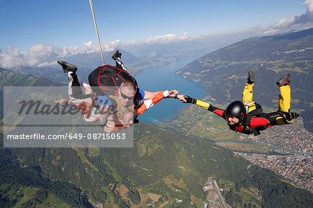 Smiling tandem sky divers holding hand with free faller, Interlaken, Berne, Switzerland
