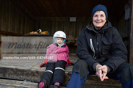 Girl wearing skiing helmet sitting on barn step with grandmother, Gavle, Sweden