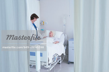 Female doctor talking to senior female patient in hospital bed Female doctor talking to senior female patient in hospital bed