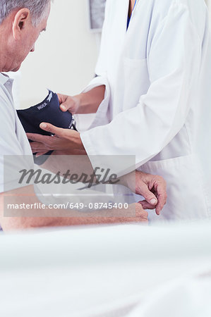 Cropped shot of female doctor using blood pressure gauge on senior male patient on hospital bed Cropped shot of female doctor using blood pressure gauge on senior male patient on hospital bed