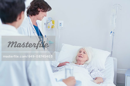 Doctors explaining to senior female patient in hospital bed