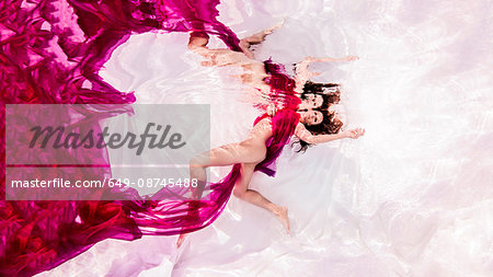 Underwater view of woman draped in sheer fabric, floating towards water surface