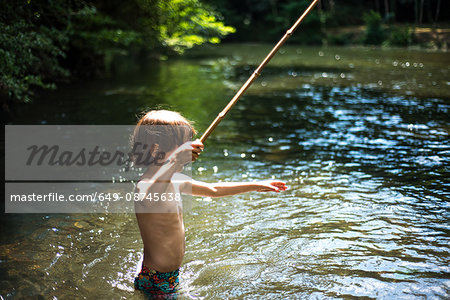 Boy waist deep in water holding stick