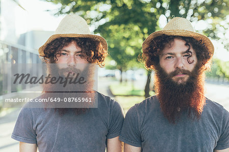 Portrait of identical male hipster twins wearing straw hats on sidewalk