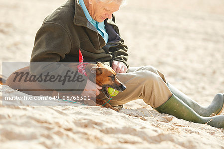 Man and dog sitting on beach, Constantine Bay, Cornwall, UK
