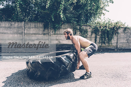 Young male cross trainer lifting heavy tyre outside gym