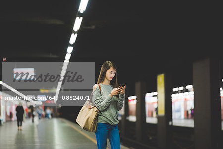 Young woman using smartphone  on railway platform at night