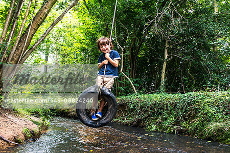 Boy on tyre using over river