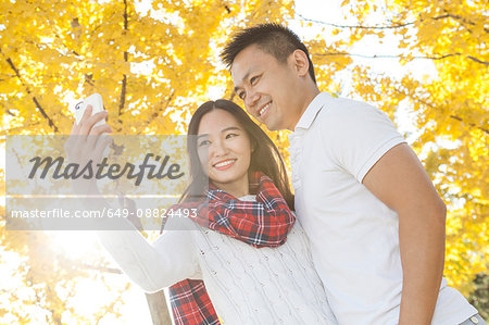 Young couple taking smartphone selfie in autumnal park, Beijing, China