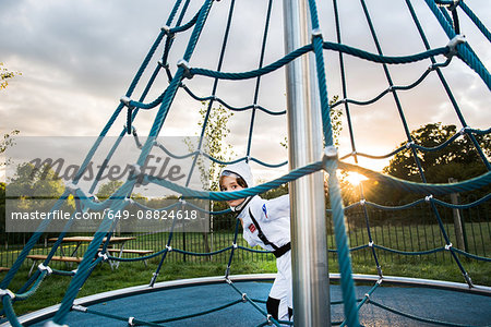 Portrait of boy in astronaut costume hiding and peering from playground climbing frame