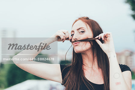 Portrait of young woman with freckles making mustache with long red hair