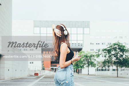 Young woman listening to headphones with hand on head outside office building