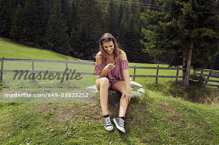 Young woman sitting in field reading smartphone texts, Sattelbergalm, Tyrol, Austria