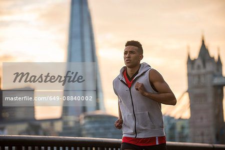 Man running by riverside, Tower Bridge and The Shard in background, Wapping, London, UK
