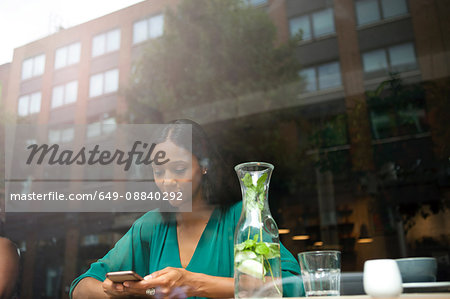 Mid adult woman reading smartphone texts in cafe window seat