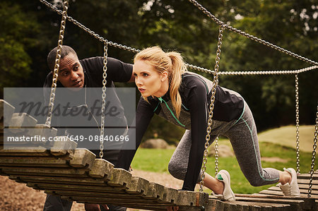 Personal trainer instructing young woman crawling on playground equipment in park