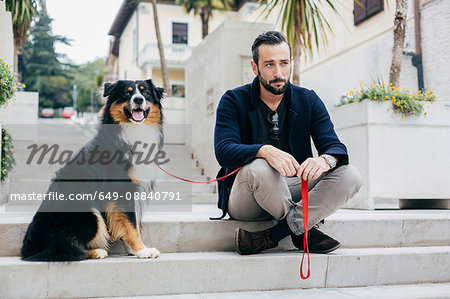 Mid adult man sitting on stairway with pet dog in city square