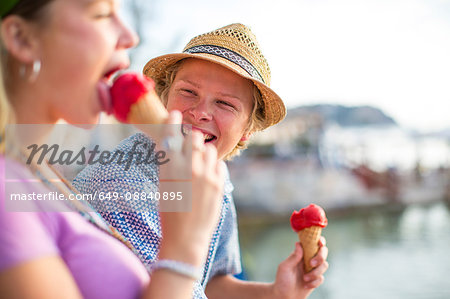 Young couple laughing and eating ice cream cones on waterfront, Majorca, Spain