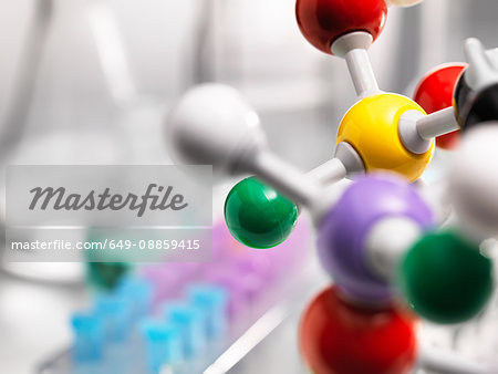 A molecular model of a chemical formula with laboratory equipment in the background