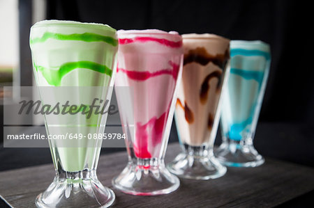 Row of four colourful milkshakes on table