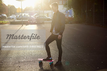 Young male skateboarder with skateboard on sunlit street