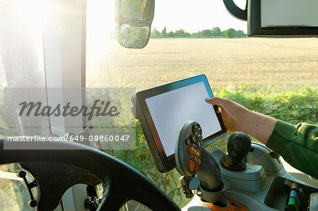 Farmer's hand driving tractor using touchscreen on global positioning system