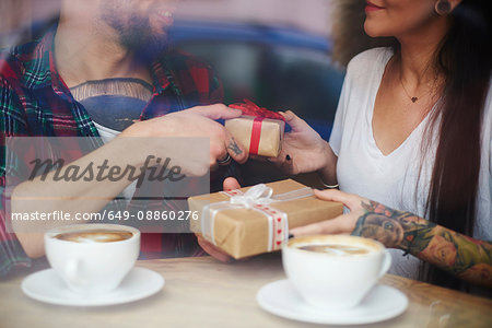 View through window of couple in coffee shop exchanging gifts