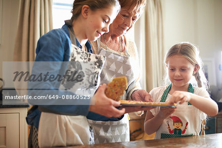 Senior woman and granddaughters picking freshly baked Christmas tree cookies