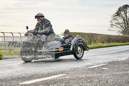 Senior man and grandson riding motorcycle and sidecar along rural road