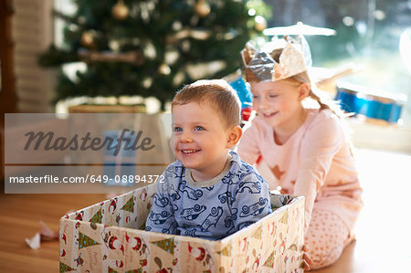 Girl pushing brother in cardboard box at christmas