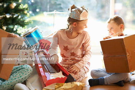 Boy and sister sitting on living room floor opening christmas gifts