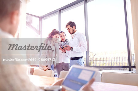 Over shoulder view of young businessman and women looking at smartphone in office