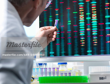 DNA Research, Scientist holding up a DNA sample with results on the computer screen DNA Research, Scientist holding up a DNA sample with results on the computer screen