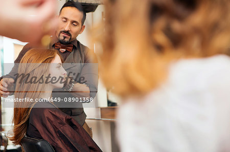 Male hairdresser styling customer's red hair in hair salon