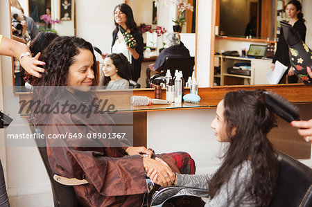 Girl and mother holding hands while having their hair styled in hair salon